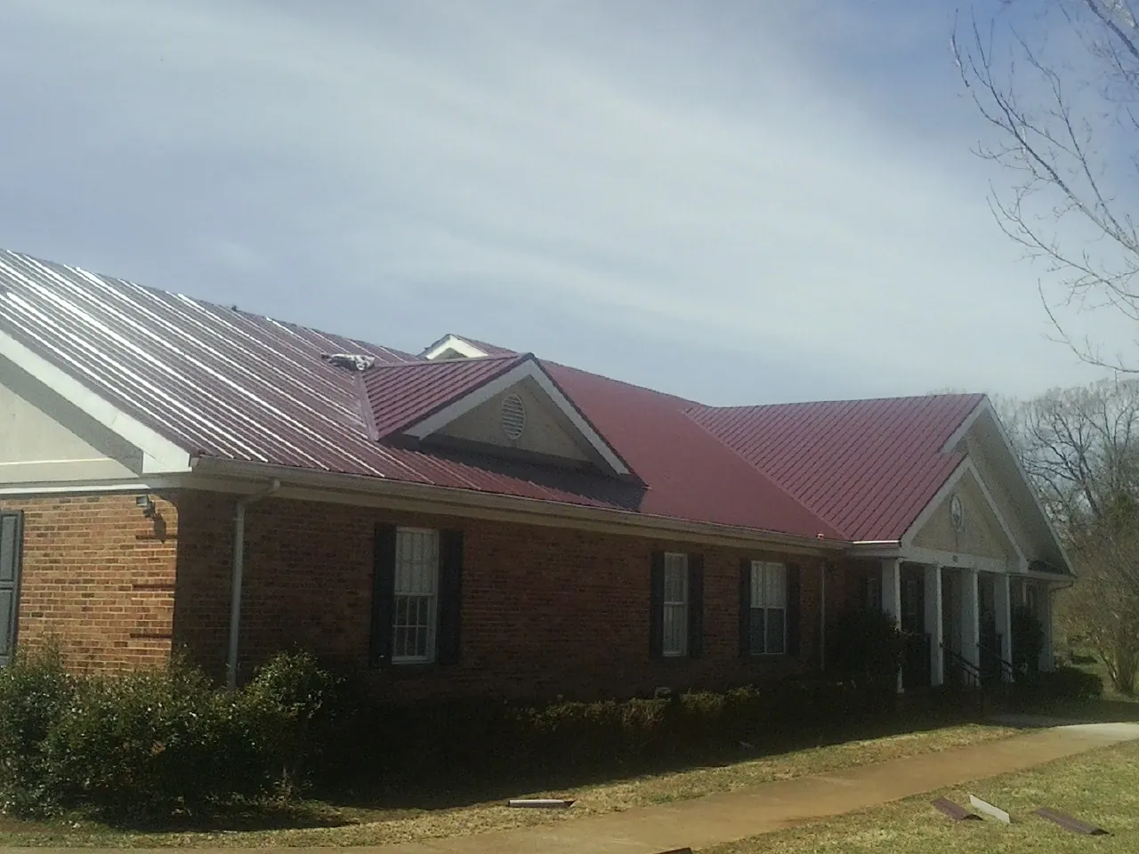Red metal roof with gabled entries on a long brick building, from a Hail Damage Roof Repair job in Mccleary