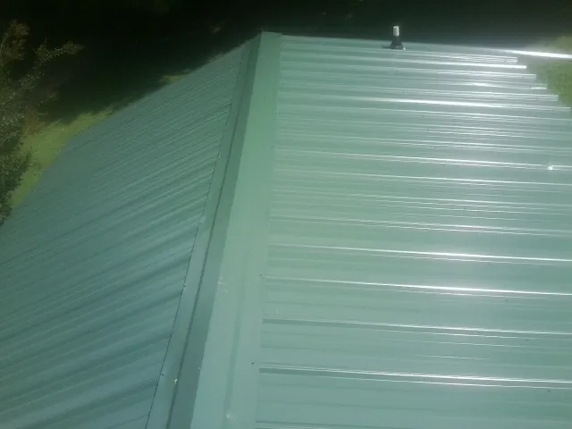 New green metal panels meeting at the ridge of a roof — Flat Roof Repair work by our crew in Mccleary