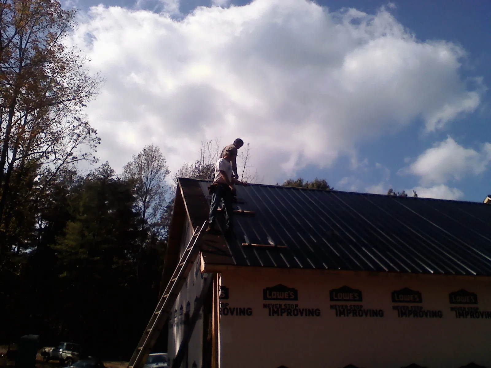 Roofer fastening dark metal panels high against a cloudy sky, from a Roof Inspection job in Mccleary
