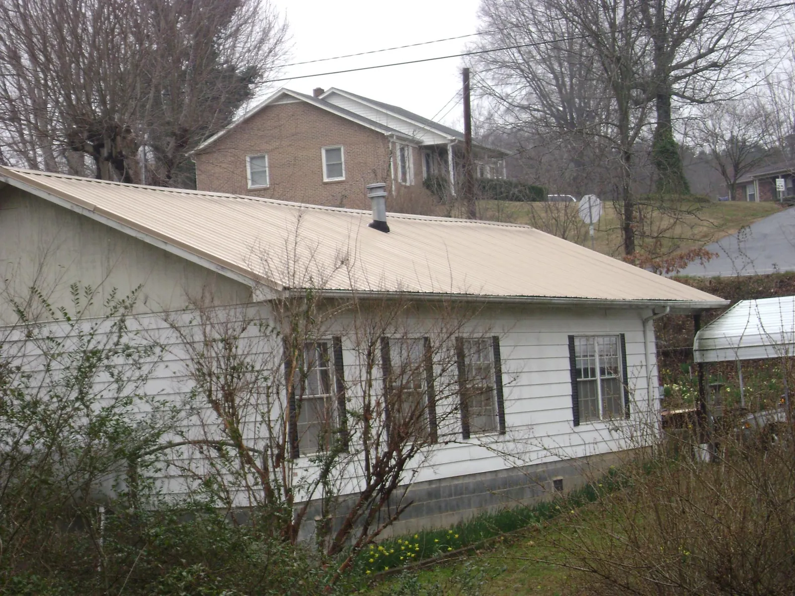Tan metal roof on a white sided house set into a hillside — Commercial Roofing by Roofing Brothers in Mccleary